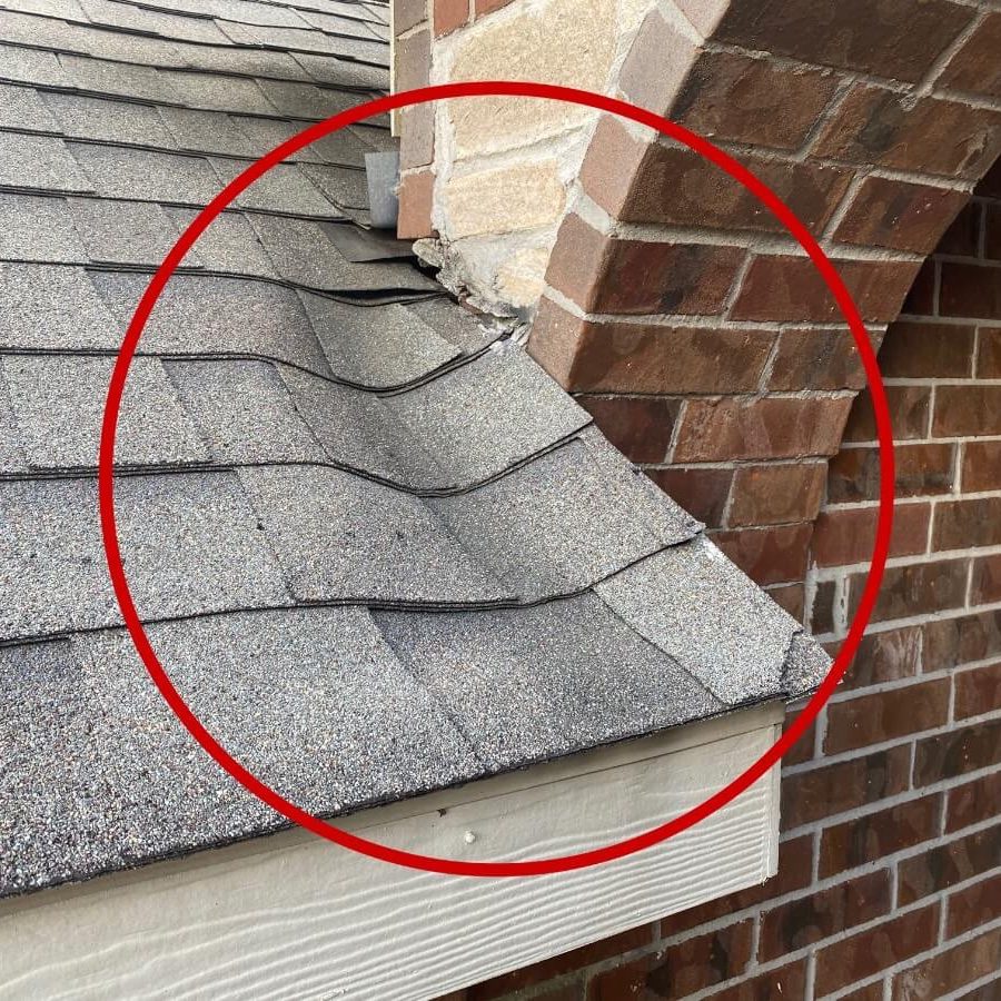 Close-up of a textured asphalt shingle roof showing a corner and brick wall detail seen during roofing maintenance.